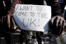 A migrant holds a placard which reads "I want to come to the UK" on his bicycle at the makeshift camp called "The New Jungle" in Calais