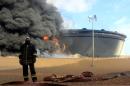 A Libyan fireman stands in front of smoke and flames rising from an oil storage tank at an oil facility in northern Libya's Ras Lanouf region on January 23, 2016