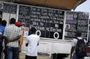Bystanders read the headlines illustrating the battle over the holding of elections in Liberia amid the Ebola crisis at a street side chalkboard newspaper in Monrovia