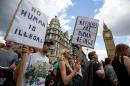 Demonstrators hold placards as they pass the Houses of Parliament during a pro-refugee rally in central London on September 12, 2015