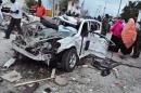 People stand by a destroyed car near the damaged Jazeera Palace hotel following a suicide attack in Mogadishu on July 26, 2015