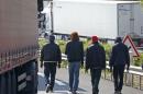 Migrants walk near trucks blocked on a road which leads to the Channel Tunnel terminal in Coquelles near Calais