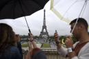 Tourists take pictures in the rain in front of the Eiffel Tower on August 8, 2014, in Paris