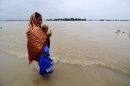 A woman carrying her child walks along a flooded road near Ashigarh in India's northeastern state of Assam