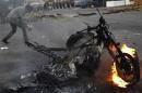 An anti-government demonstrator walks behind a burning motorcycle during a protest in San Cristobal