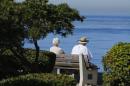 An elderly couple looks out at the ocean as they sit on a park bench in La Jolla, California