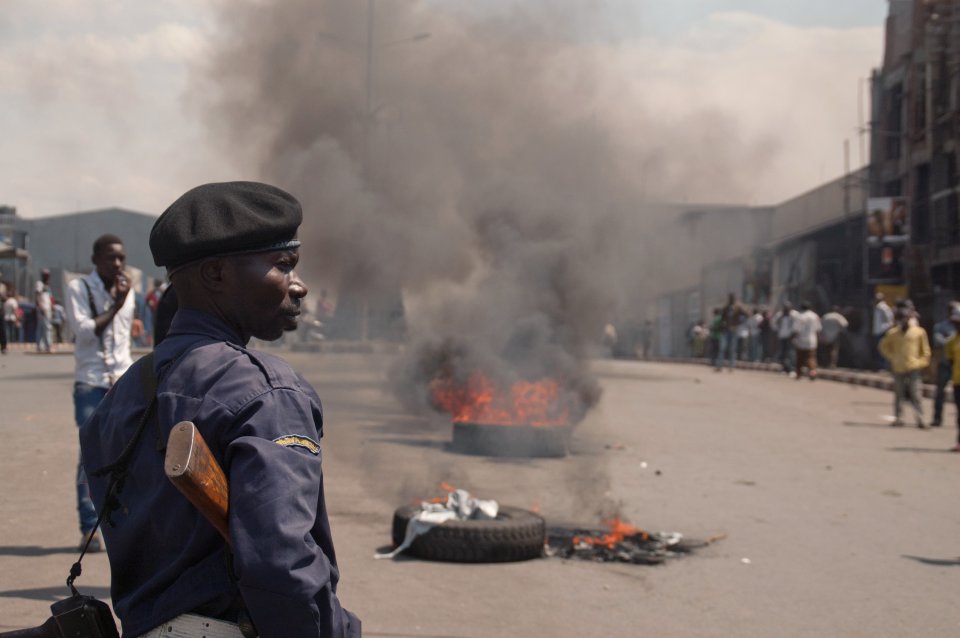 A police officer looks on as protestors burn tires in the street following recent violence, including mortar attacks that have struck homes and churches in the eastern provincial capital, killing at least seven civilians and wounding dozens of others, in Goma, Congo, Saturday, Aug. 24, 2013. Congolese soldiers supported by U.N. forces fought rebels in the country's deteriorating east for hours early Saturday, officials said, while a rocket landed inside the town of Goma and killed three people. Congo immediately blamed the attacks on neighboring Rwanda, which has long been accused of supporting the eastern Congolese rebel movement known as M23. (AP Photo/Joseph Kay)