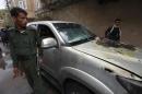 Policemen stand by a damaged car where a French man was assassinated, in Sanaa