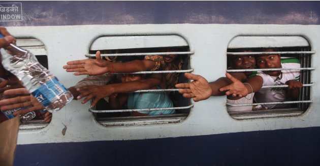 People from India&#39;s northeastern states raise their hands through windowpanes to collect free food at a railway station in Kolkata