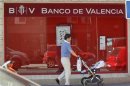 A man pushes a pram past a Banco de Valencia bank branch in Madrid
