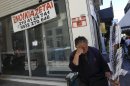 A lottery vendor stands outside a closed shop with a rental sign on it in Piraeus