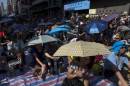 Protesters sit under umbrellas at a main street at Mongkok shopping district after thousand of protesters blocked the road in Hong Kong