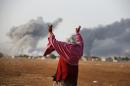 Syrian Kurd Kiymet Ergun, 56, gestures, in Mursitpinar on the outskirts of Suruc, at the Turkey-Syria border, as thick smoke rises following an airstrike by the US-led coalition in Kobani, Syria as fighting continued between Syrian Kurds and the militants of Islamic State group, Monday, Oct. 13, 2014. Kobani, also known as Ayn Arab, and its surrounding areas, has been under assault by extremists of the Islamic State group since mid-September and is being defended by Kurdish fighters. (AP Photo/Lefteris Pitarakis)