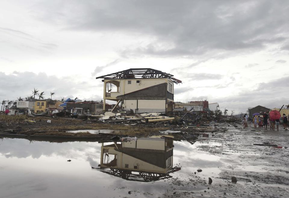 Survivors walk past damaged houses at typhoon ravaged Tacloban city, Leyte province, central Philippines on Tuesday, Nov. 12, 2013. The Philippines emerged as a rising economic star in Asia but the trail of death and destruction left by Typhoon Haiyan has highlighted a key weakness: fragile infrastructure resulting from decades of neglect and corruption. (AP Photo/Aaron Favila)