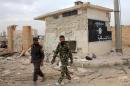 Syrian government forces walk past a building bearing an Islamic State group flag in Jabboul after taking control of the village from IS group militants on October 24, 2015