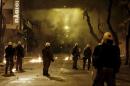 Riot police stand guard during clashes with hooded youth seen in Athens