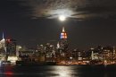 A full moon rises behind the Empire State Building and the skyline of New York, as seen from a park along the Hudson River in Hoboken, New Jersey