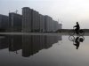 Man cycles past a residential complex under construction, which is reflected in a puddle, in Taiyuan