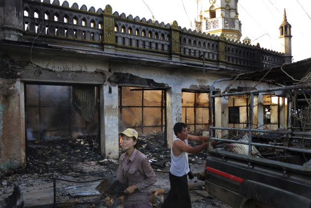 In this May 29, 2013 photo, Ma Sandar Soe, left, salvages goods from her burned shop in the foreground of a vandalized mosque in Lashio, northern Shan State, Myanmar. When a huge mob of Buddhist thugs crawled on the roof of Ma Sandar Soe's shop, doused it with gasoline and set it ablaze, the Buddhist businesswoman didn't blame them for burning it to the ground despite seeing it happen with her own eyes. Instead, her wrath was reserved for minority Muslims she accused of igniting Myanmar's latest round of sectarian unrest. (AP Photo/Todd Pitman)