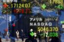 People are reflected in a display showing the Nikkei average and the NASDAQ average of the U.S outside a brokerage in Tokyo