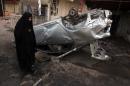 An Iraqi woman walks past the wreckage of a car that was destroyed by an explosion in Baghdad's northern Shiite-majority district of Sadr City, on April 17, 2014