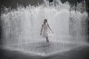A girl stands surrounded by the jets of a fountain on the South Bank on a hot summer day in central London