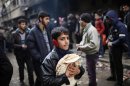 File photo of a boy holding pita bread as others stand in line outside a bakery in Aleppo