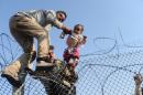 In this photo taken by Bulent Kilic a Syrian child fleeing the war is lifted over a border fence to enter Turkish territory illegally, near the border crossing at Akcakale in Turkey's Sanliurfa province, June 14, 2015