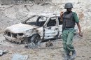 A Somali soldier walks near a destroyed car near the entrance of Mogadishu's court complex, Mogadishu, Somalia, Sunday, April 14, 2013. Militants launched a serious and sustained assault on Mogadishu's main court complex Sunday, detonating at least two blasts, taking an unknown number of hostages and exchanging extended volleys of gunfire with government security forces, witnesses said.(AP Photo/Farah Abdi Warsameh)