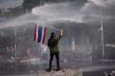 An Anti-government protester waves Thai National Flag under water cannon fired by police during a protest in Bangkok, Thailand, Monday, Dec. 2, 2013. After a weekend of chaos in pockets of Bangkok, protesters vowed to push ahead with plans to topple Prime Minister Yingluck Shinawatra by occupying her office compound along with other key government buildings. Police again used tear gas on thousands of protesters on Monday after repeatedly driving them back with similar attacks throughout Sunday. (AP Photo/Vincent Thian)