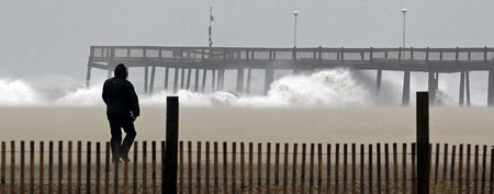 A man walks the beach as waves from the Atlantic Ocean crash into the pier in Ocean City, Maryland October 28, 2012. (REUTERS/Kevin Lamarque)